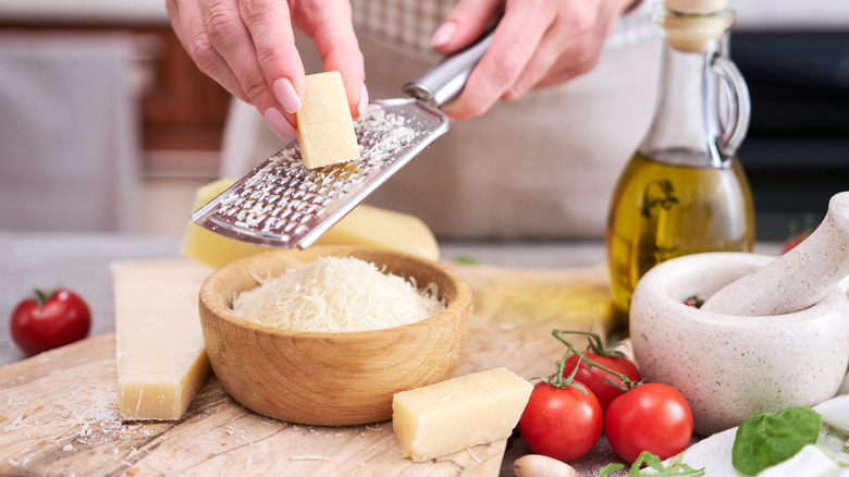 Person grating Parmesan cheese into a wooden bowl