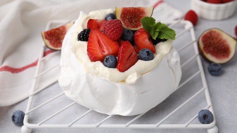 a pavlova topped with mixed berries resting on a wire rack