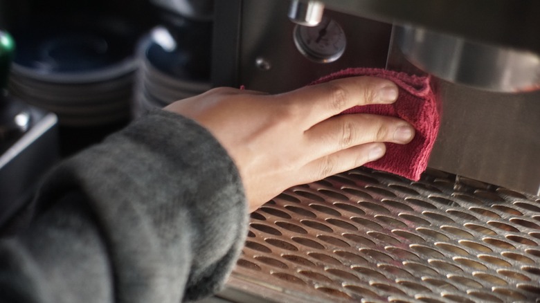 Hand cleaning an espresso machine with a red cloth