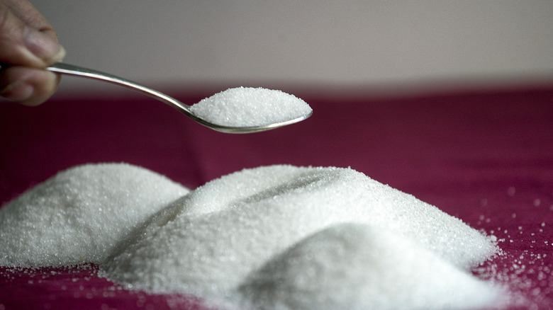 Three piles of refined sugar on a red tablecloth with a hand holding a spoonful of sugar above them.