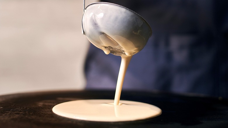 Pancake batter dripping off ladle into skillet