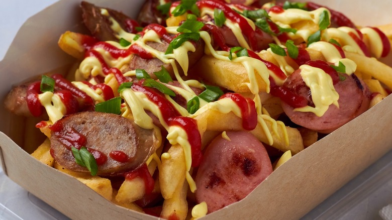 Salchipapas in a cardboard boat with ketchup,  mustard, and green onions