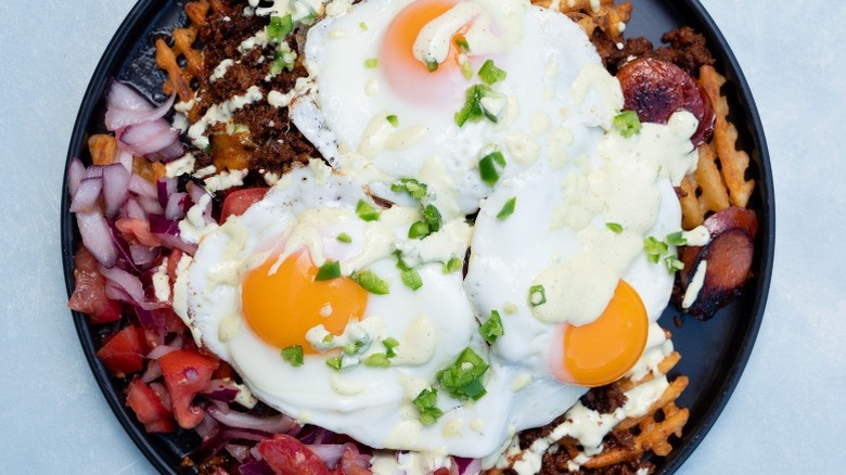 Salchipapas Mexicana topped with chorizo, eggs, red onions, tomatoes, and green onions