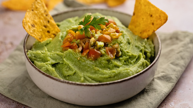 bowl of guacamole with two nachos dipped inside and garnished with salsa