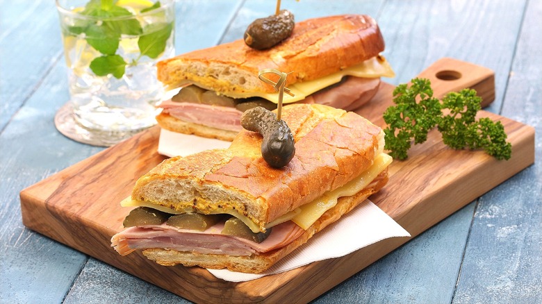 Halved Cuban sandwich held together with toothpicks on wooden cutting board