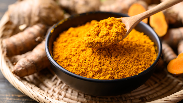 Powdered turmeric in a bowl and whole turmeric root