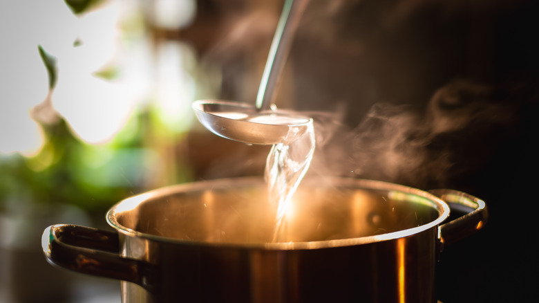 A ladel being held above a pot of soup on a stove.