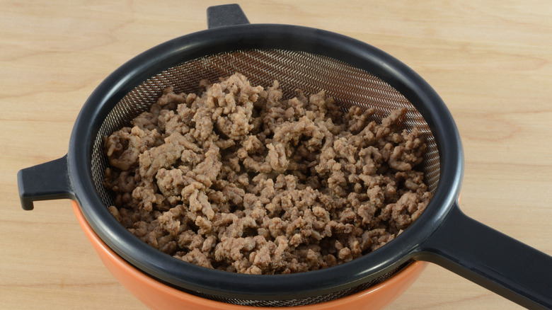 Straining ground beef over a bowl