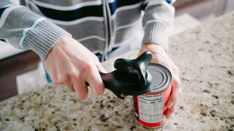 person opening a can of food with a can opener