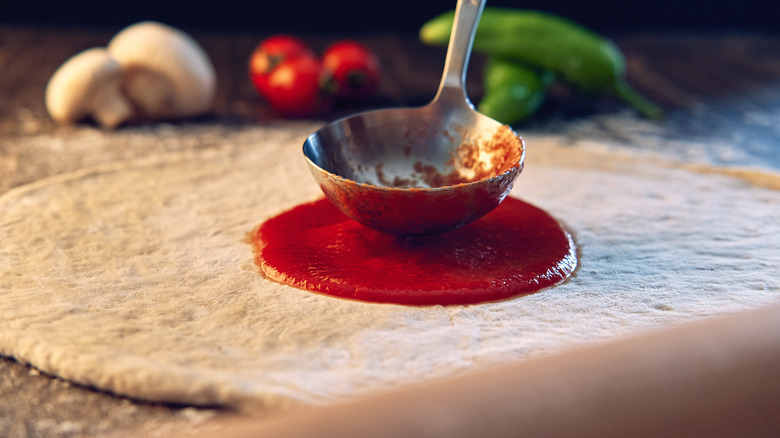 Ladle spreading red sauce on pizza dough