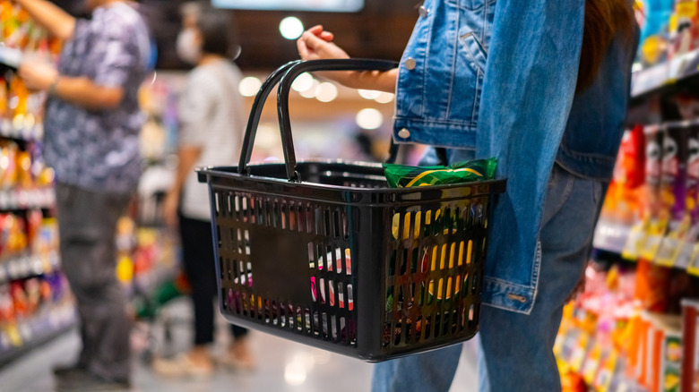 Person holding a basket in a grocery store aisle