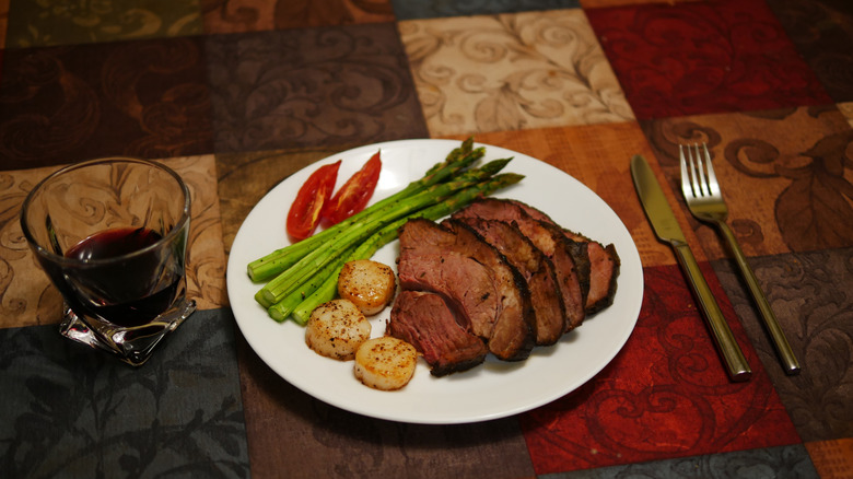 Meat with asparagus on white plate next to glass of red wine