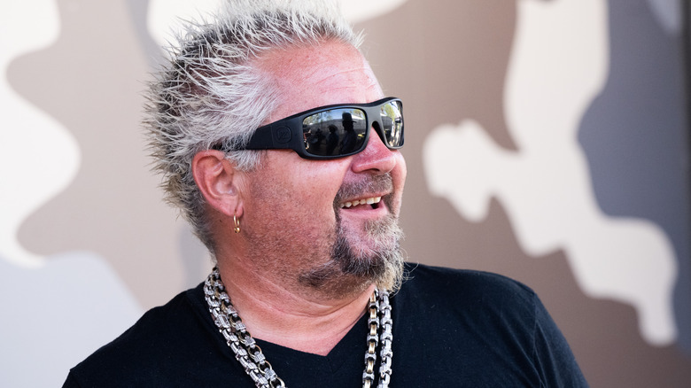 Guy Fieri smiling in sunglasses at an event