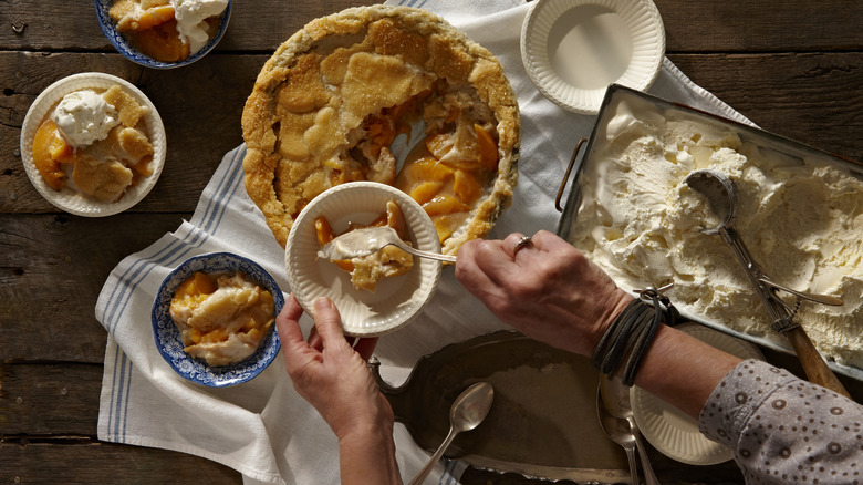 Person spooning vanilla ice cream into bowls of peach pie