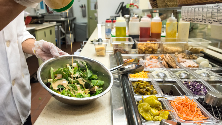 Chef pouring dressing into a bowl of salad