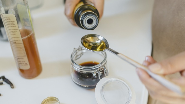 Person pouring oil into a jar of vinaigrette