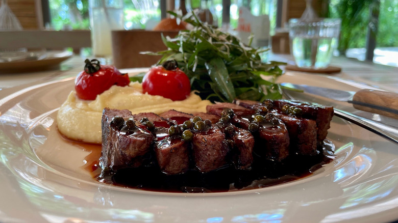 A drizzled cut of steak and mashed potatoes on a plate beside a salad