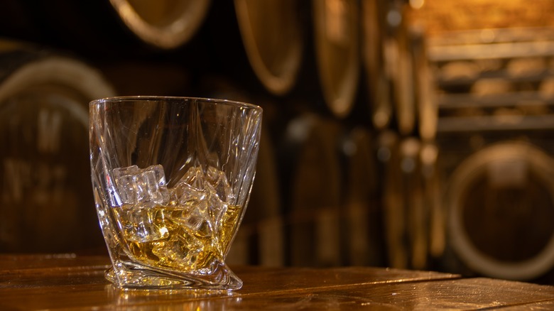 Glass of whiskey with ice with barrels in the background