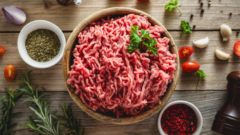 Ground beef in a bowl with herbs and spices around it.