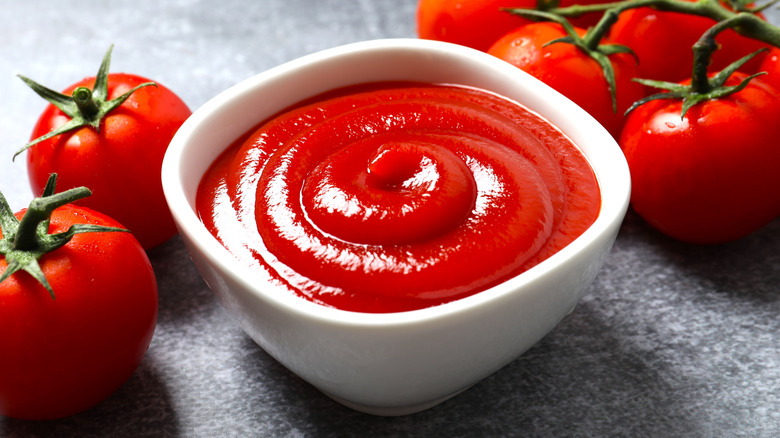 A bowl of ketchup next to fresh tomatoes