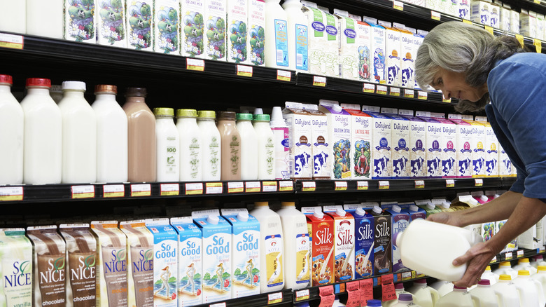 Woman holding a gallon of milk in front of milk aisle.