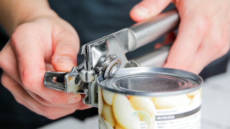 Closeup of hands using a can opener to open a can of food