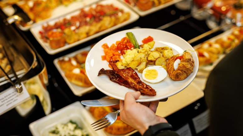 Hand holding a plate above a breakfast buffet.