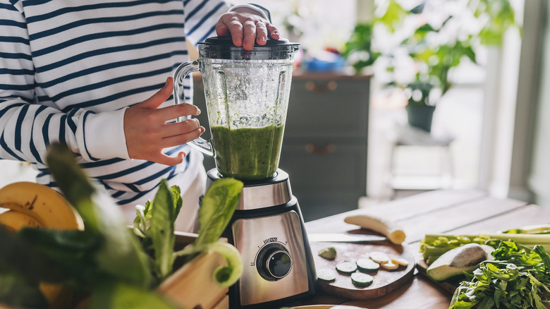 A person in a striped shirt is operating a blender.