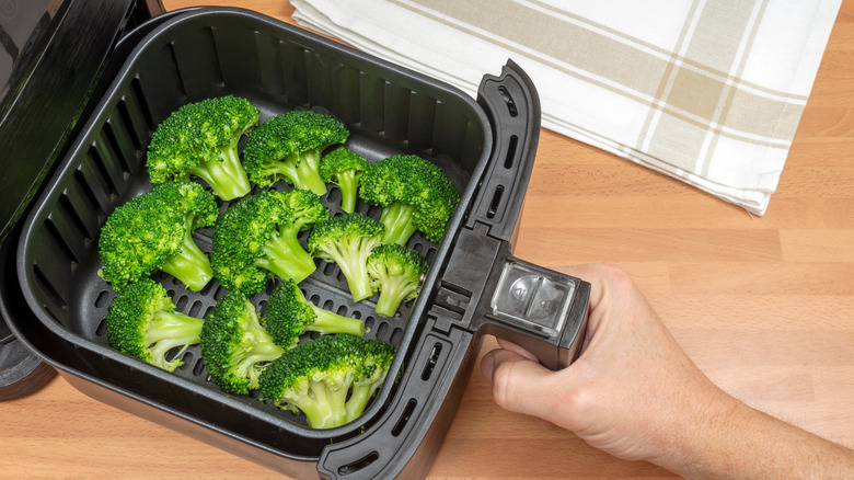 Person grabbing air fryer basket full of broccoli