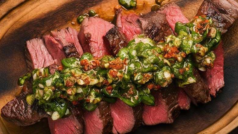 chimichurri-topped sliced skirt steak on a wooden plate