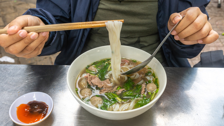 Using chopsticks and spoon while having pho noodle soup