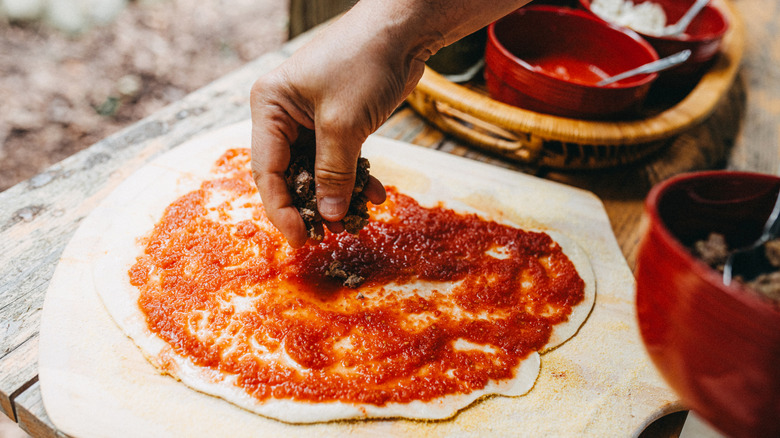 A hand placing toppings on a pizza base.