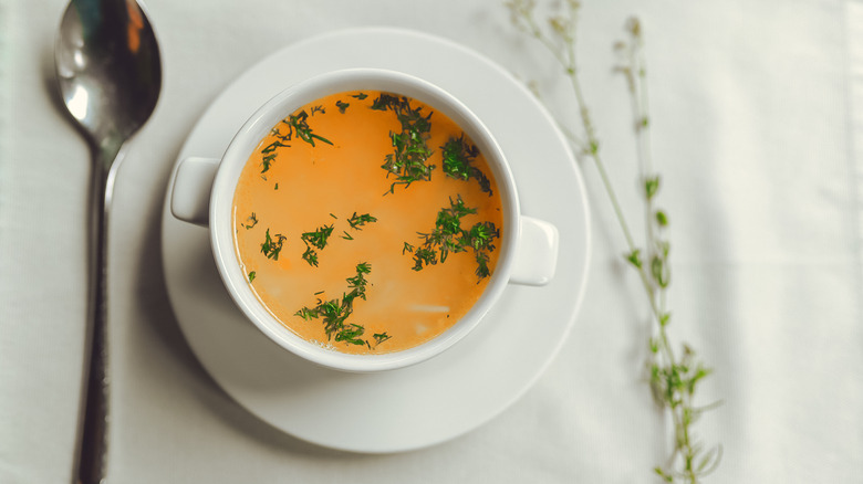 white bowl of chicken broth next to metal spoon