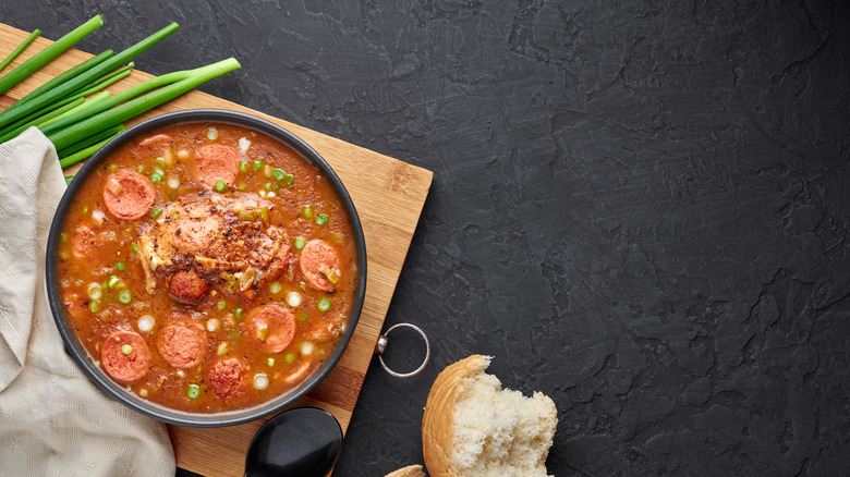 a bowl of gumbo, green onions and a piece of bread