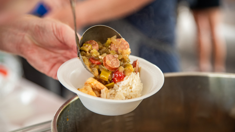 a person ladles a spoonful of gumbo on top of rice out from a big pot