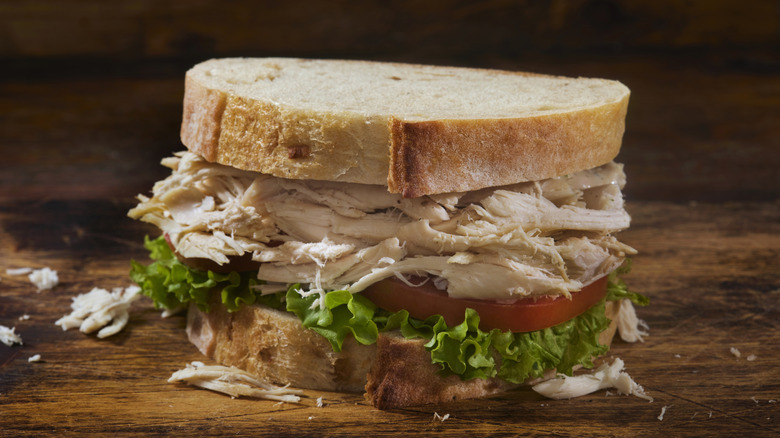 A shredded chicken sandwich on rustic sourdough bread with lettuce and tomato at the base