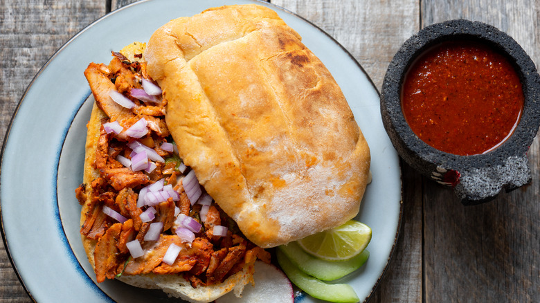 Mexican torta al pastor pork sandwich with red salsa