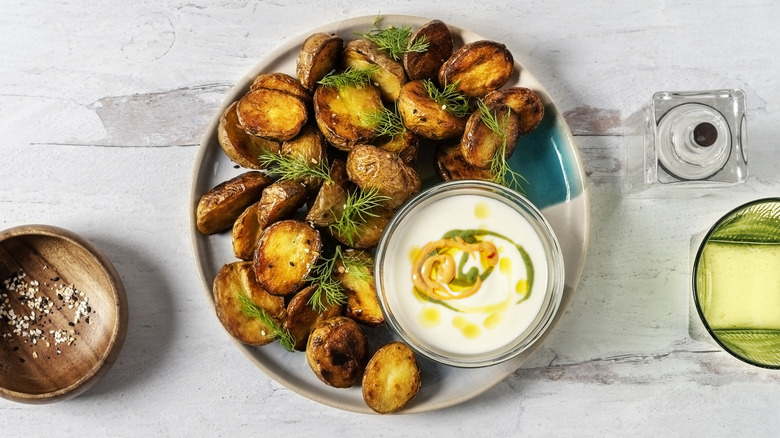 A plate of roasted potatoes with herbs and dipping sauce