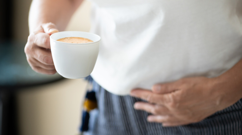 A person holding their stomach and a cup of coffee