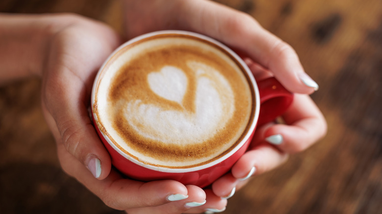 Hands holding a hot latte in a red cup