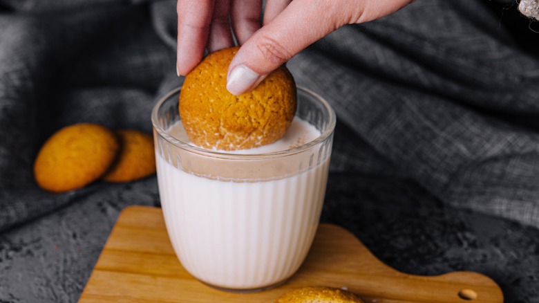 hand dipping cookie in milk