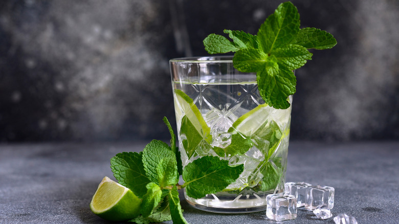 minty mojito drink with slices of lime and ice on gray background