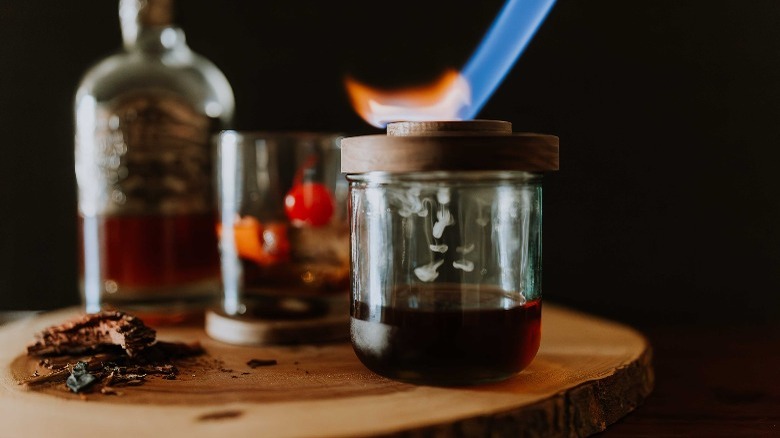 Torching a cocktail smoker lid over a glass