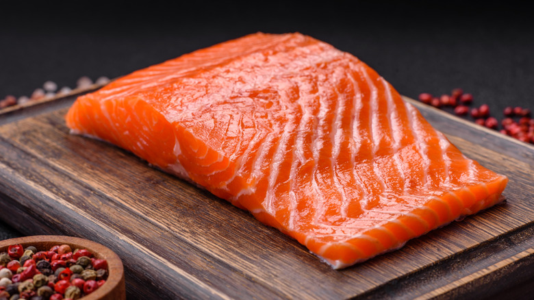 Raw salmon filet on a cutting board surrounded by seasoning