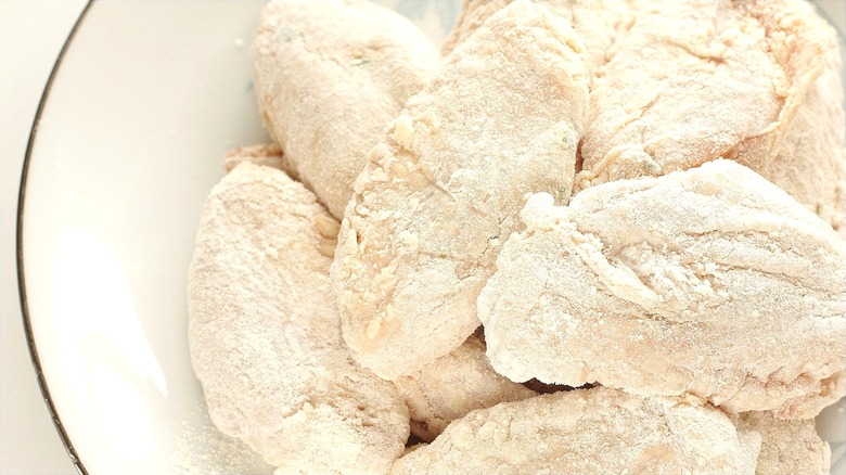 Raw chicken wings coated in flour or cornstarch on white plate