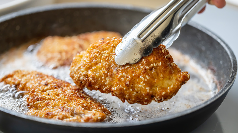 Tongs holding chicken cutlet over pan