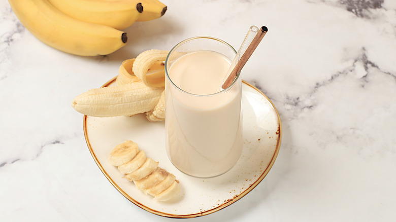 Banana milk in a glass with bananas and a straw