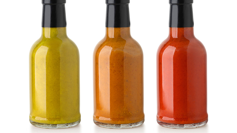 Three bottles of hot sauce of different colors sit side by side.