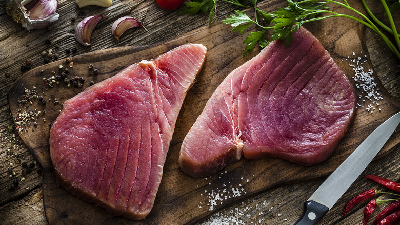 Raw tuna steaks on a cutting board beside a knife.