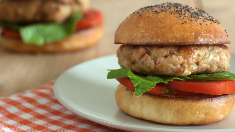 A tuna burger with lettuce and tomato on a sesame seed bun on a plate.